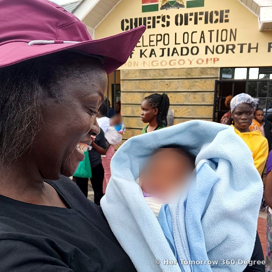 A woman smiles down at a newborn wrapped in a blue blanket